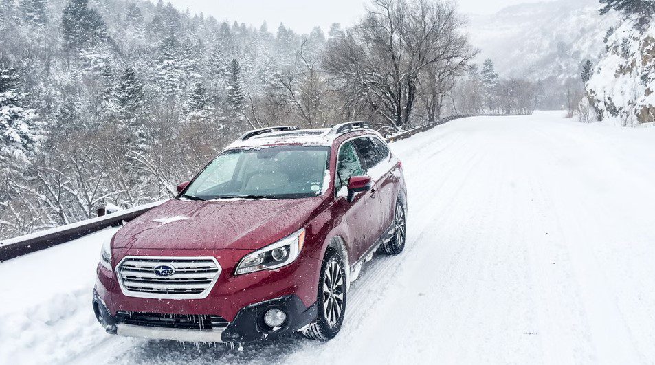 A cherry red Subaru Outback driving in heavy snow.